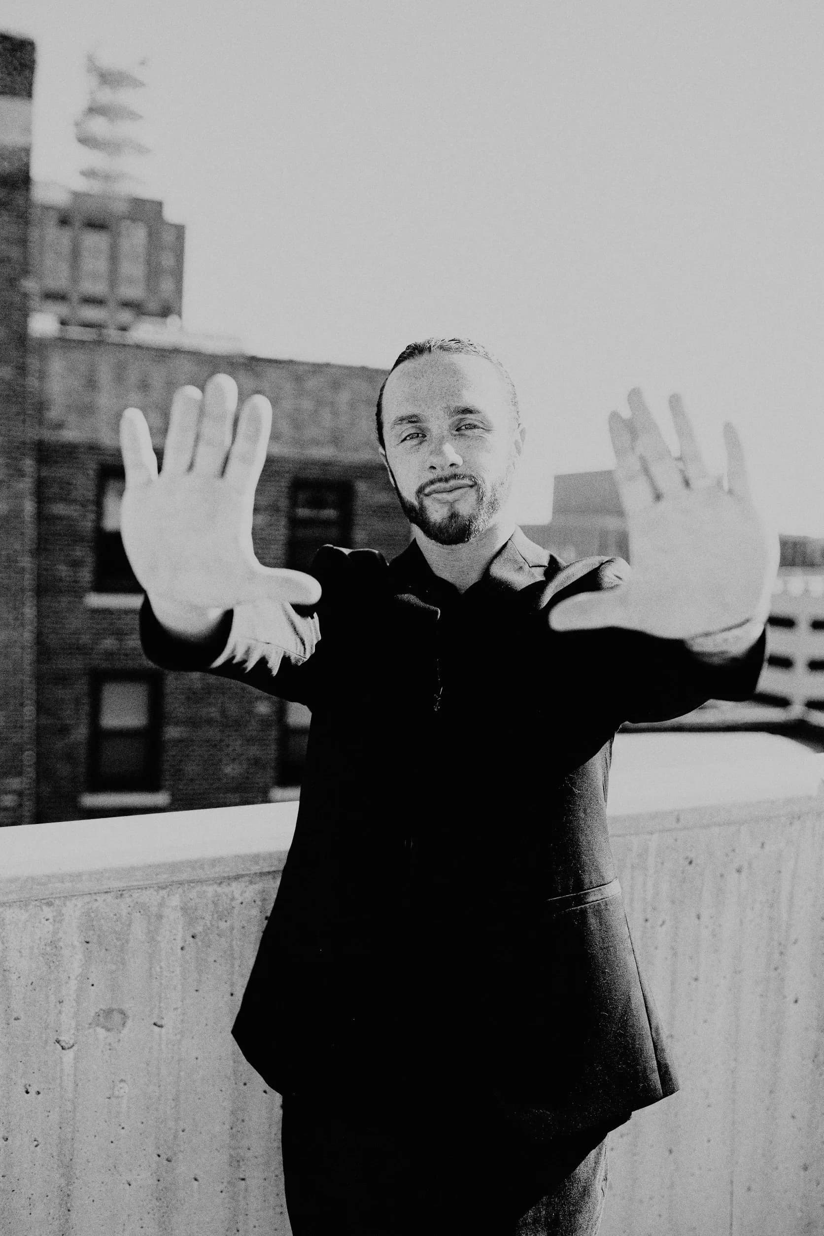Black and white portrait of Rudy Perez Jr. with both hands raised toward the camera
