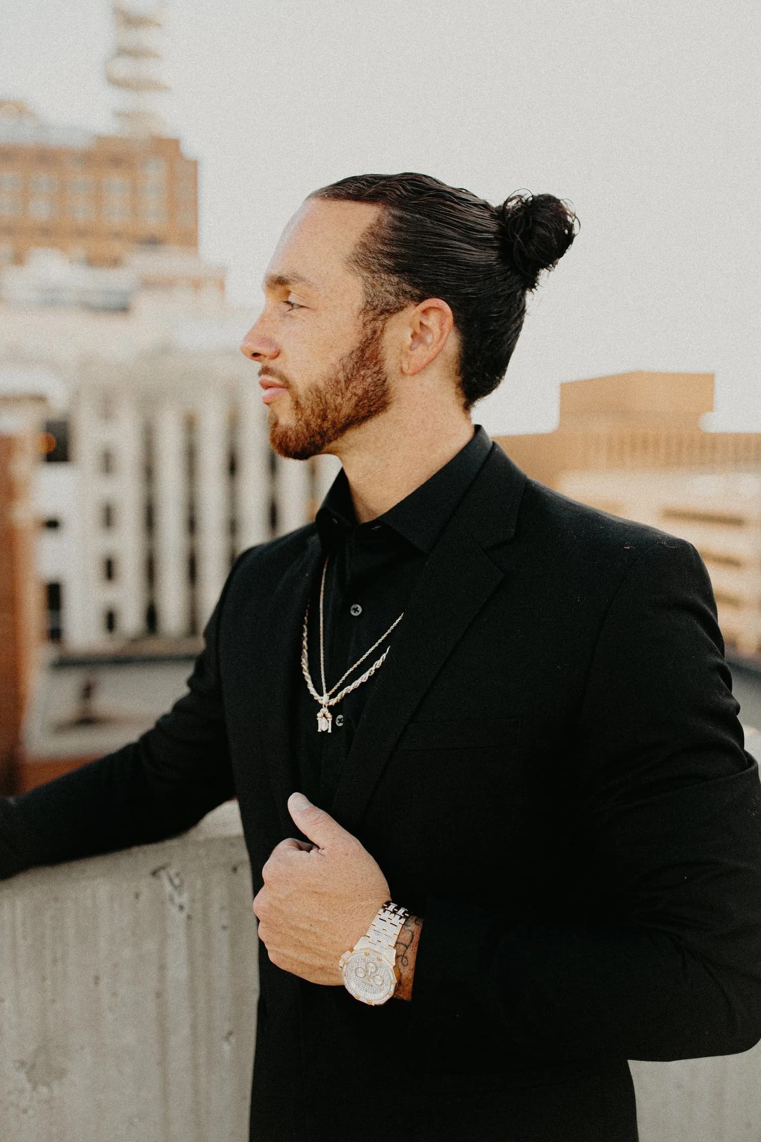 Rudy Perez Jr. in a black suit, in profile on a city rooftop